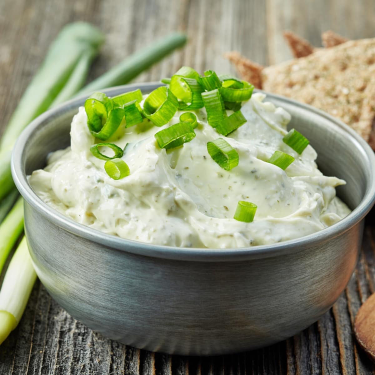 Blue Cheese Dip in a Metal Bowl Garnished With Fresh Green Onion Slices and Green Onions and Chips in the Background