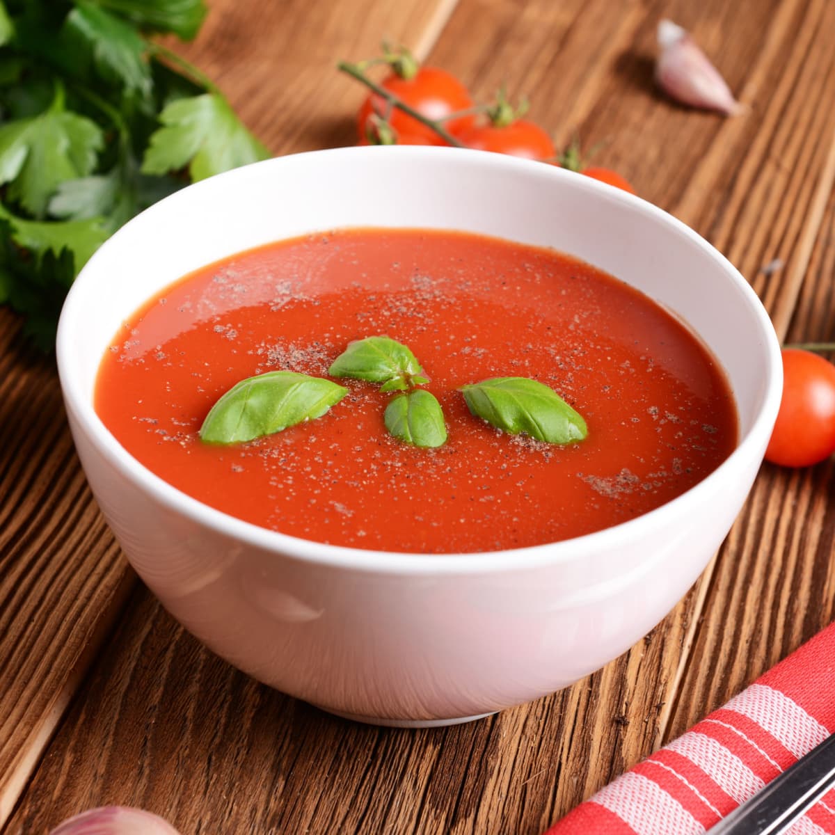 A bowl of tomato soup on top of wooden table. 