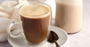 Foamy coffee on a glass mug beside a glass pitcher half filled with coconut creamer.