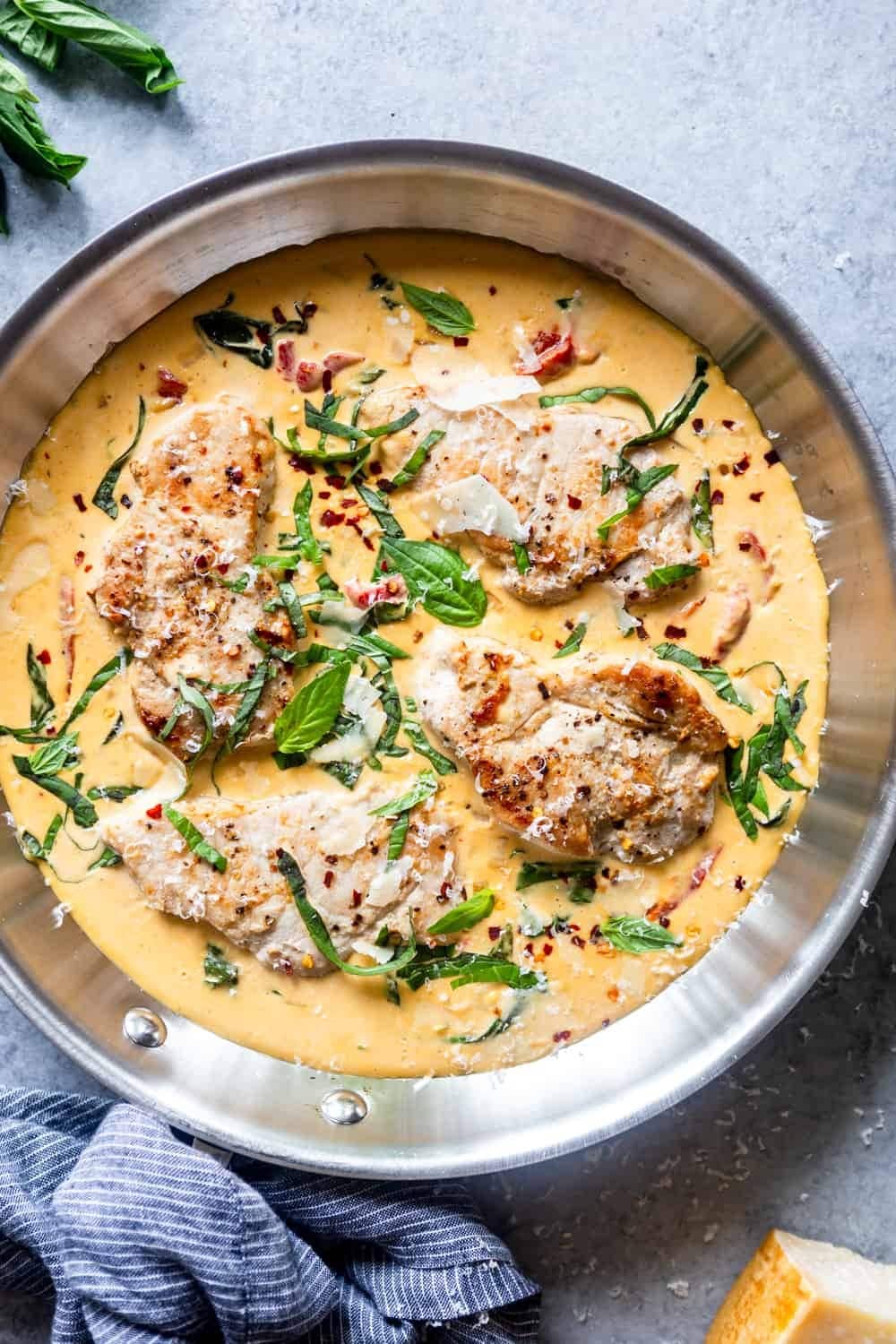 Pork chops with creamy sauce and basil cooked in a stainless skillet. 