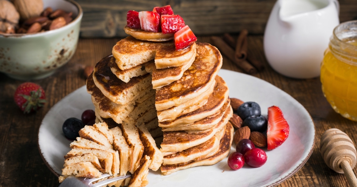 Sliced stack of pancakes on a white plate garnished with strawberry slices served on a white plate.