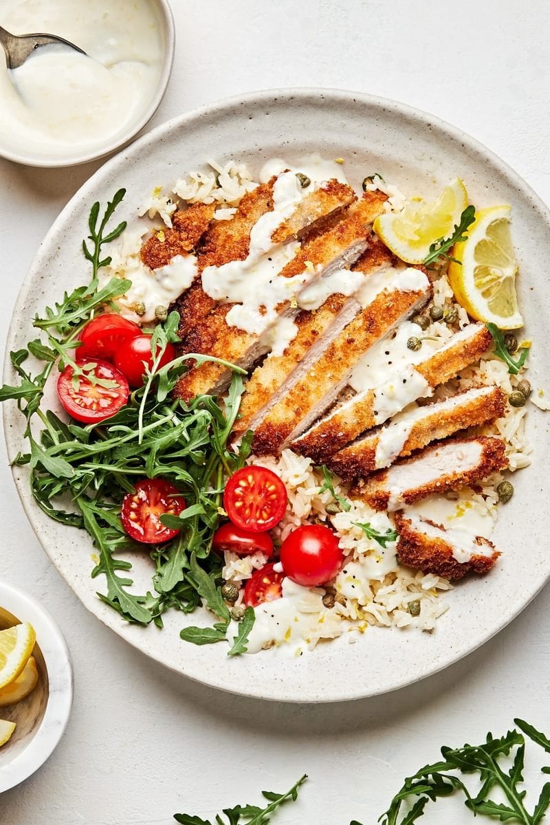 Pork Milanese bowls made with Parmesan rice, crunchy arugula, and vibrant cherry tomatoes.