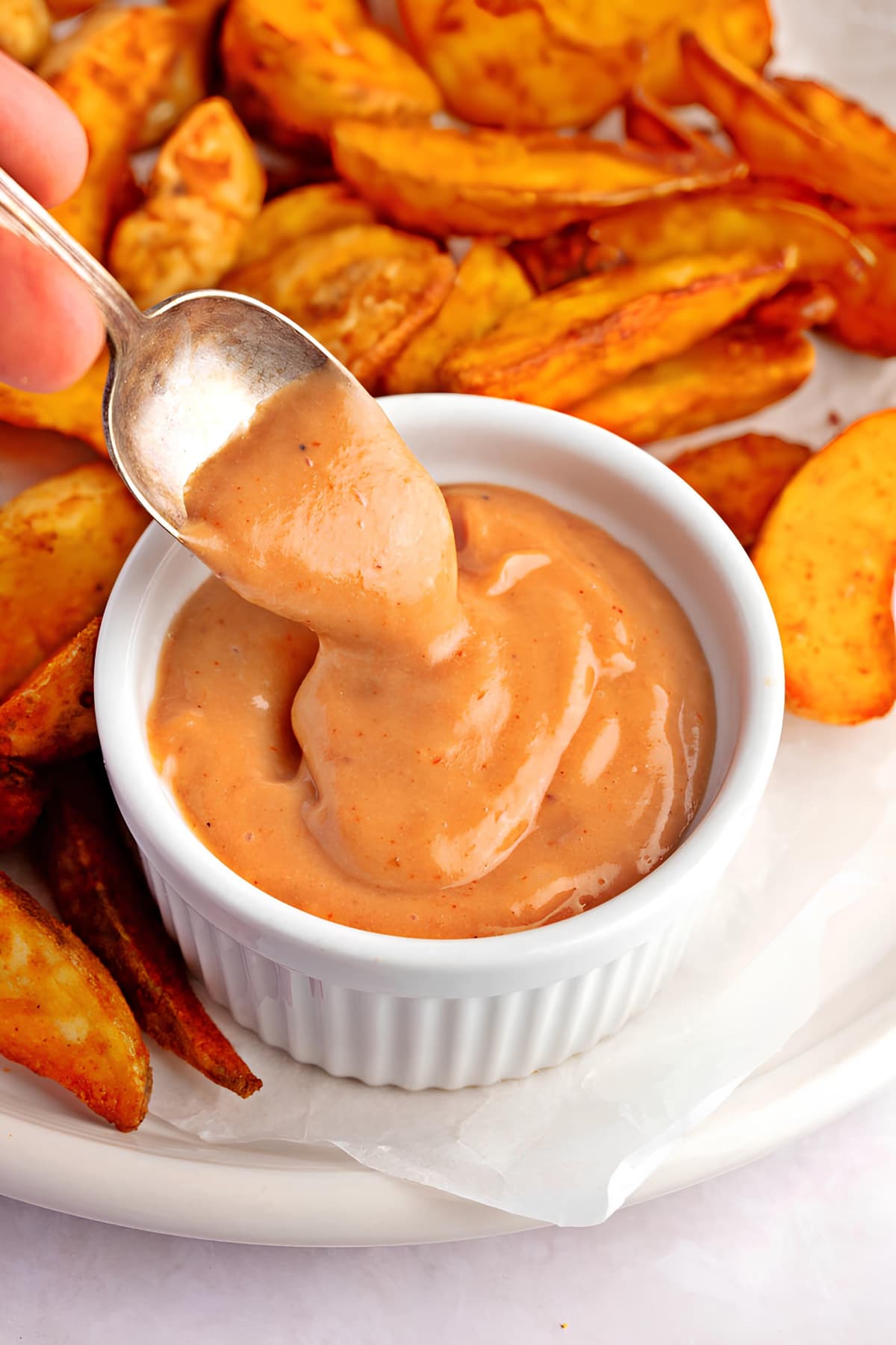 Spoon scooping on a bowl of dipping sauce made with barbecue sauce, full-fat mayo, and dried chipotle powder.