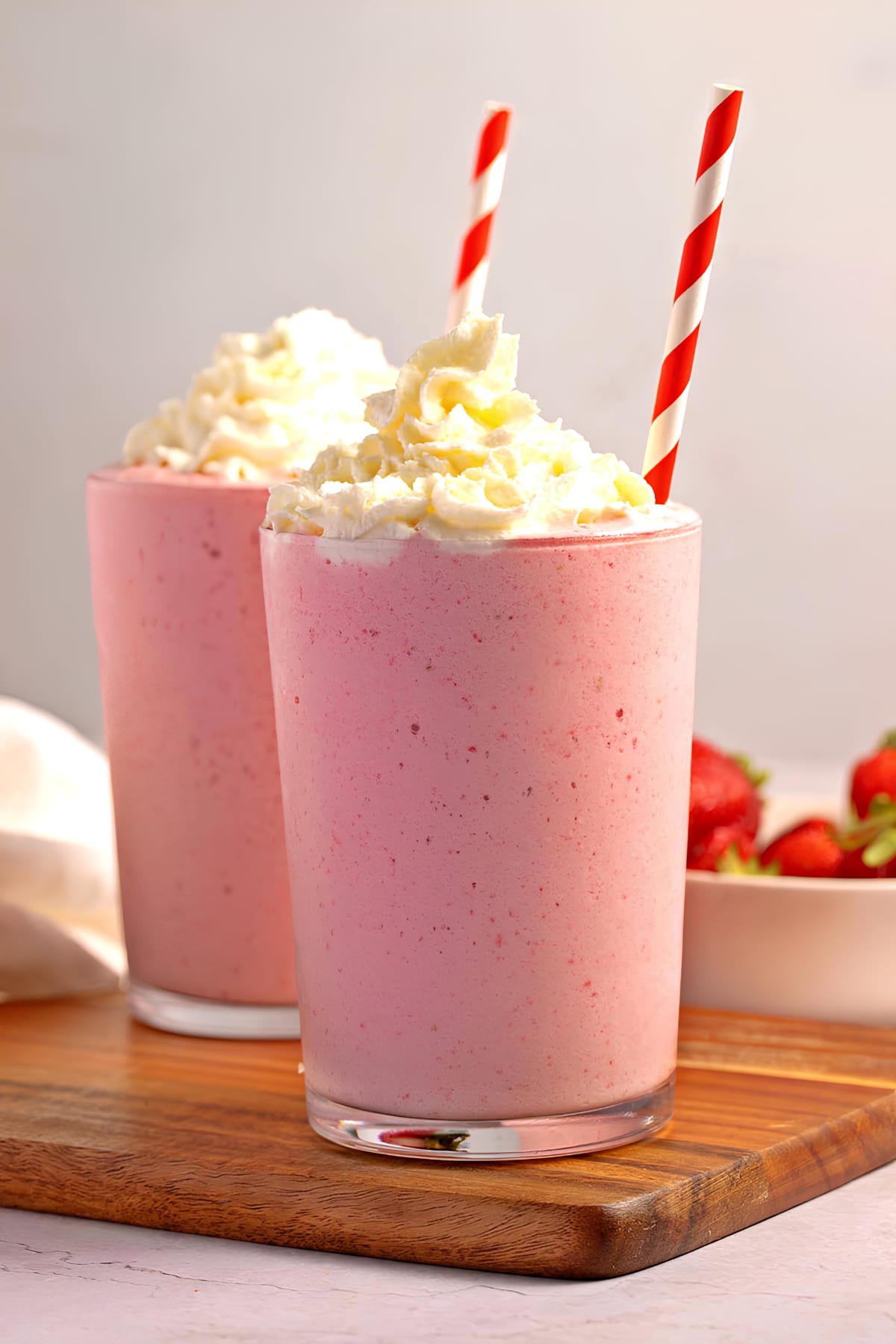 Two glasses of strawberry cappuccino with whipped cream on top served with straw. 